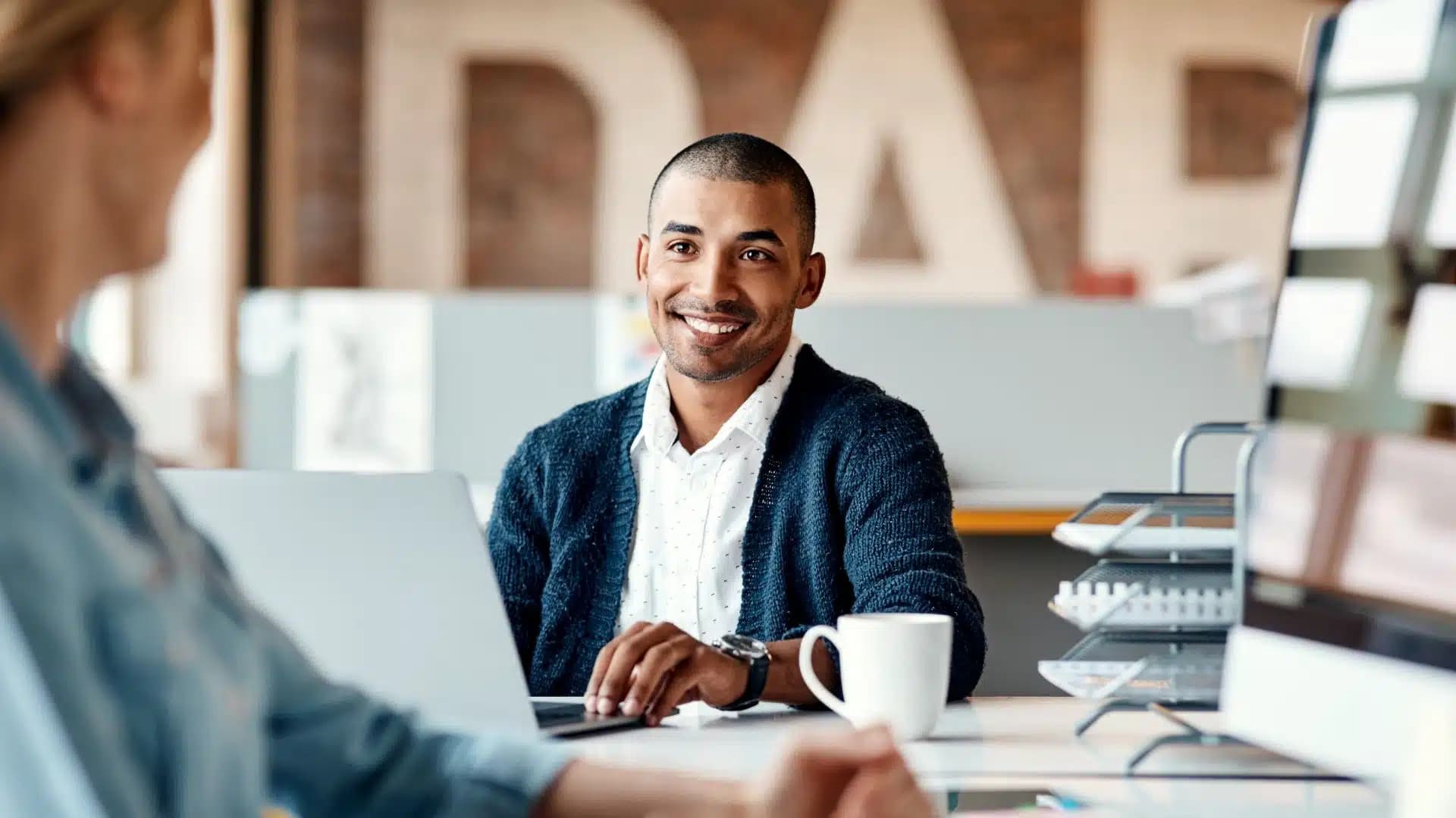 Two men sitting at a desk talking and smiling